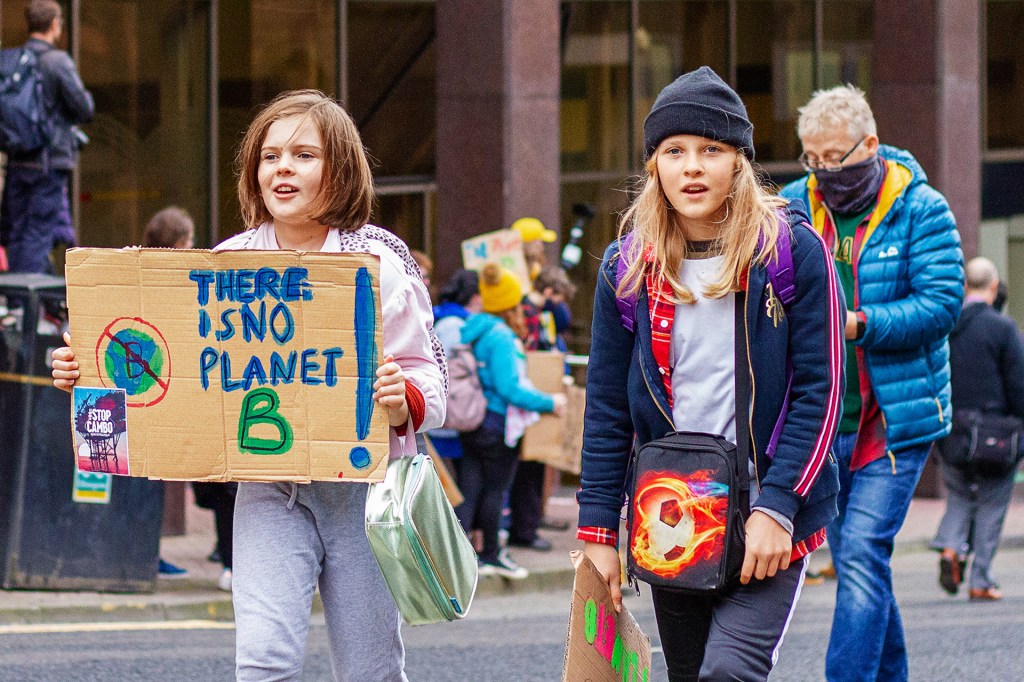 two young kids. one holding a cardbord sign with text "THERE IS NO PLANET B!". the other with beanie hat.