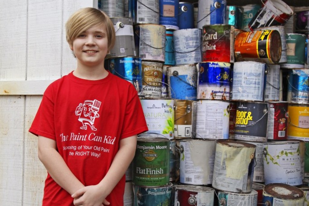 boy with red shirt standing next to stacks of empty paint cans