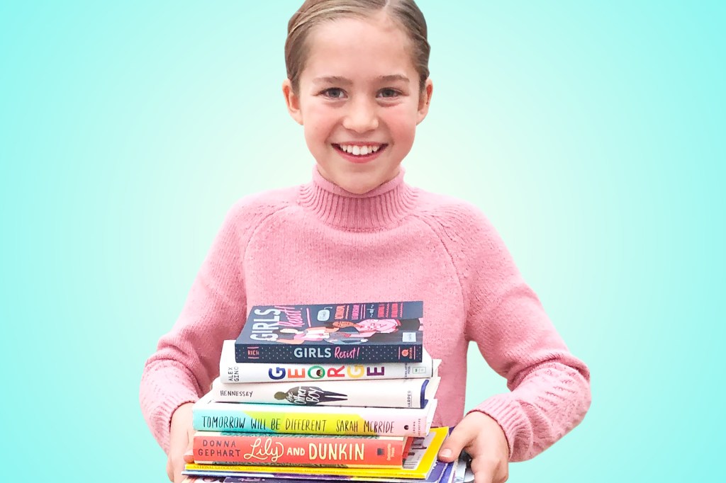 girl in pink sweater holding a pile of books in front of a light blue background