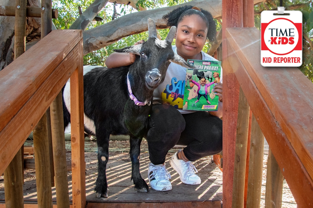 girl smiling with a book on her left hand and next to a black and white goat