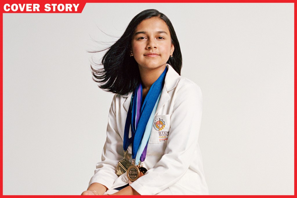 girl with white coat sitting in front of white background with several medals and awards around her neck